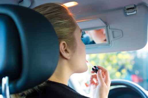 Young woman with lipstick in car looks into review mirror